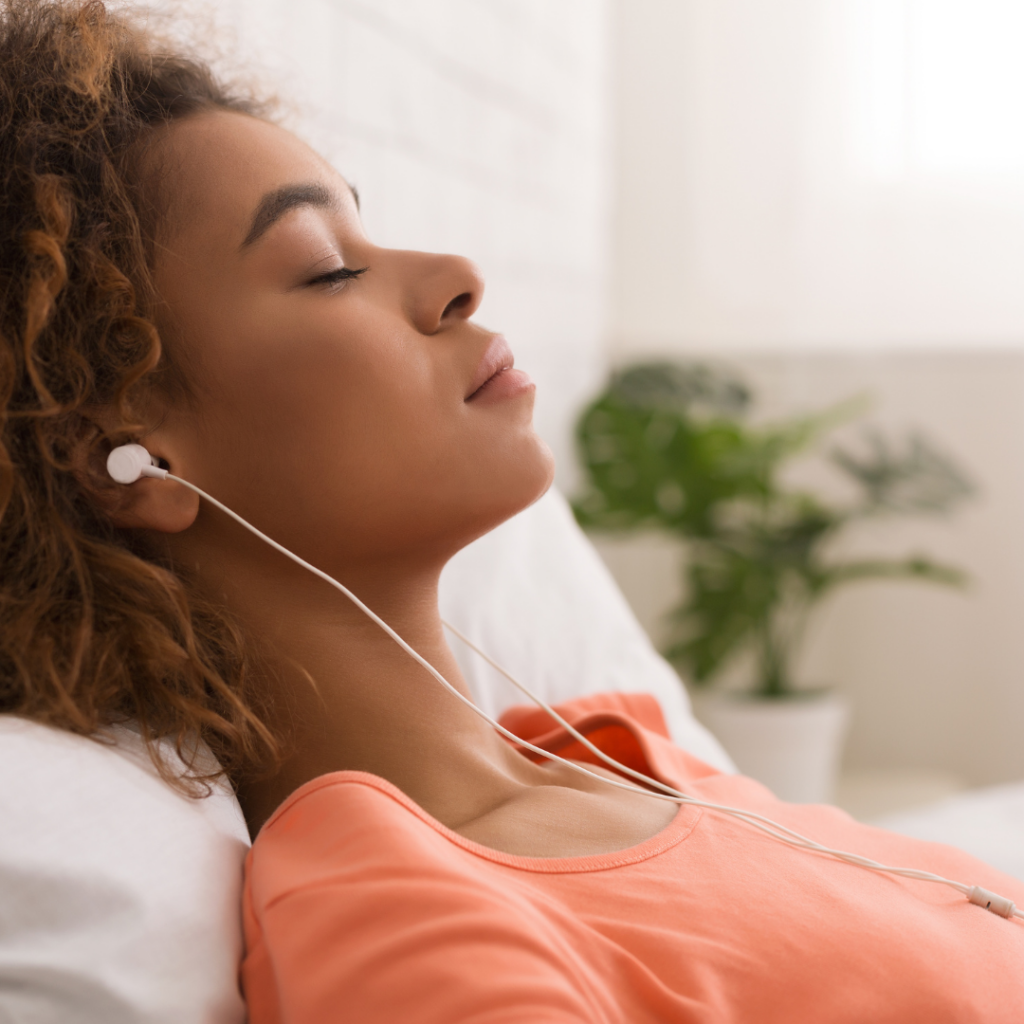 Black woman lying on the bed with headphones listening to affirmations for anxiety