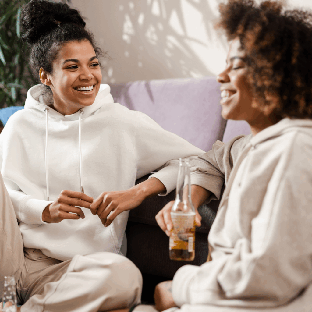 Black women laughing and talking in a home environment with drinks in their hand | How to stop being a people pleaser