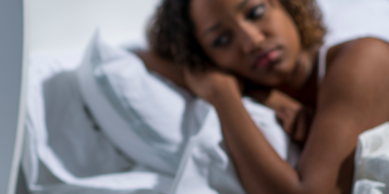 Black woman lying in bed having trouble sleeping wondering why am I tired but can't sleep