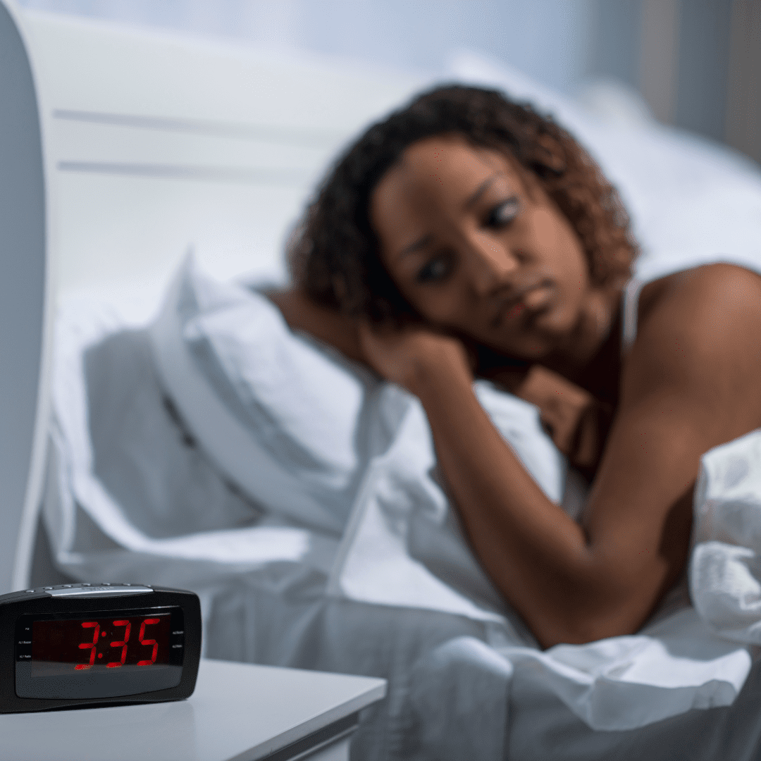 Black woman lying in bed having trouble sleeping wondering why am I tired but can't sleep