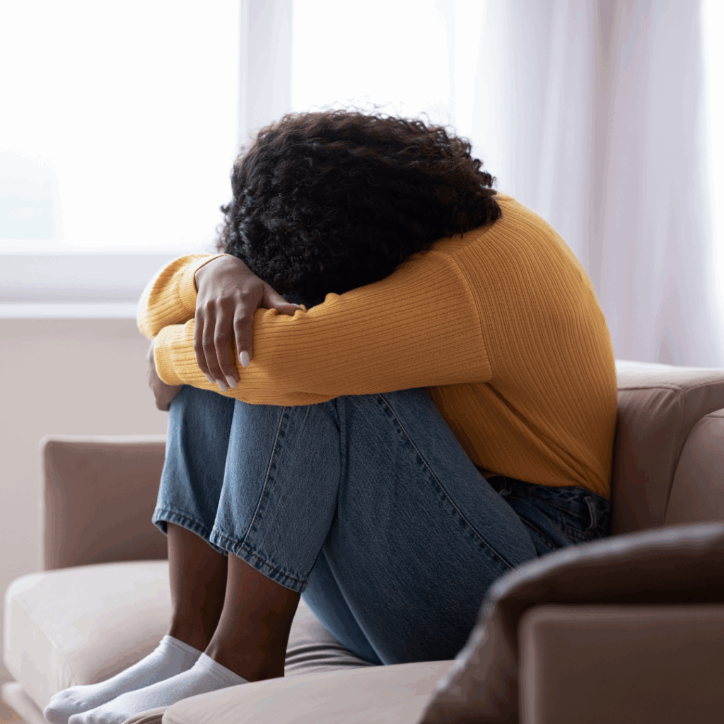 Black woman sad and alone on sofa, head in arms. How to get over a breakup
