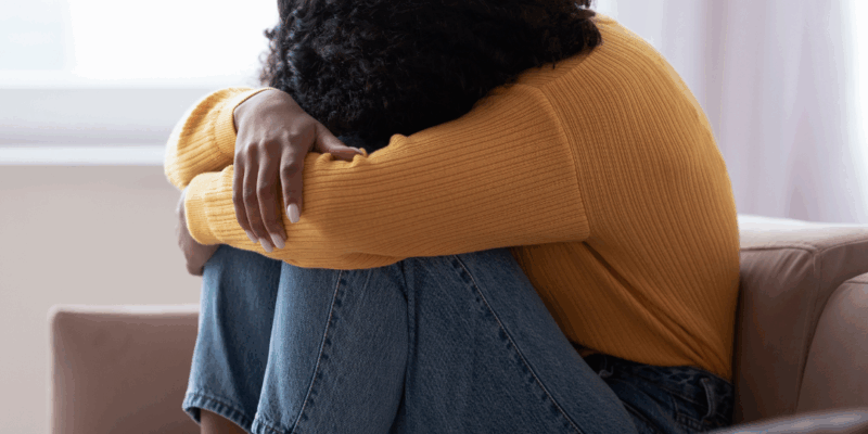 Black woman sad and alone on sofa, head in arms. How to get over a breakup