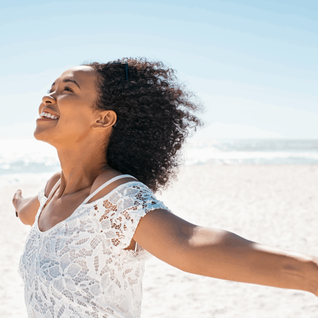 Black woman happy on the beach with arms spread out and smiling | How to live your best life
