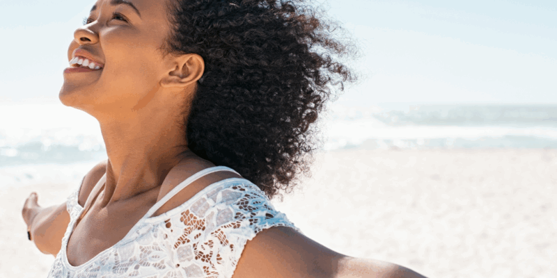 Black woman happy on the beach with arms spread out and smiling | How to live your best life