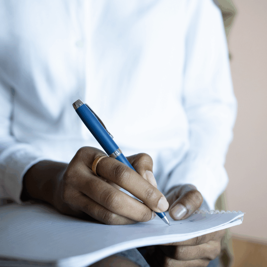 Black woman's hand writing in a notebook with a pen | journal prompts for anxiety