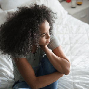 Young Black woman sitting on bed with head resting in hand | Why do I always feel alone