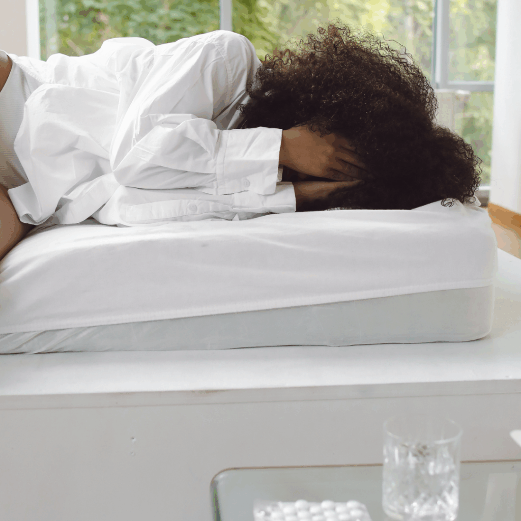 Black woman lying in bed with hands over her face, water and pain medicine near her | Depression after drinking