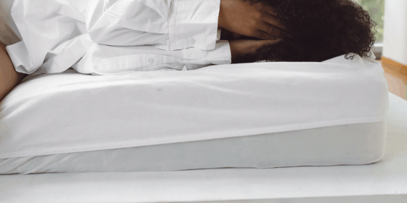 Black woman lying in bed with hands over her face, water and pain medicine near her | Depression after drinking