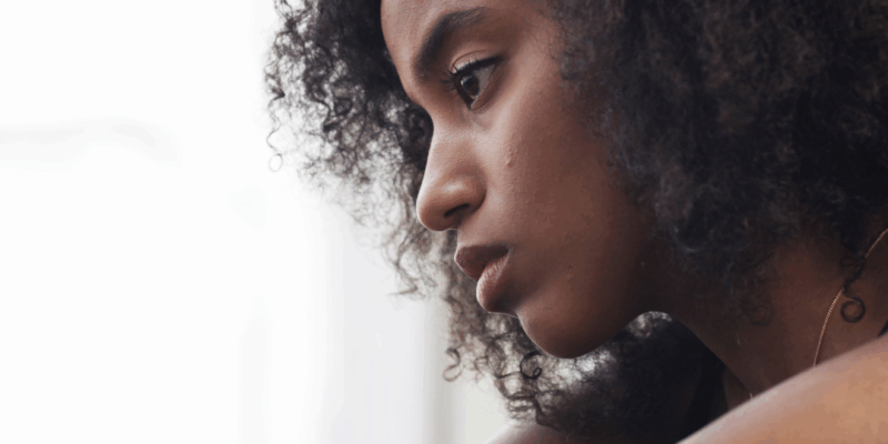 Black woman looking sad, arms hugging needs How to help a friend with depression