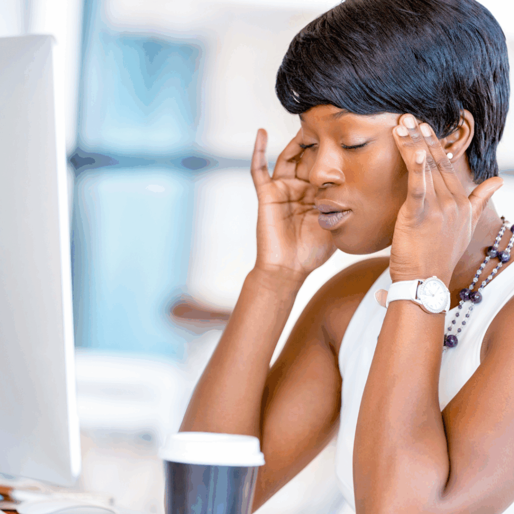 Black woman sitting at work desk, hands to temples calming down | Stress leave from work