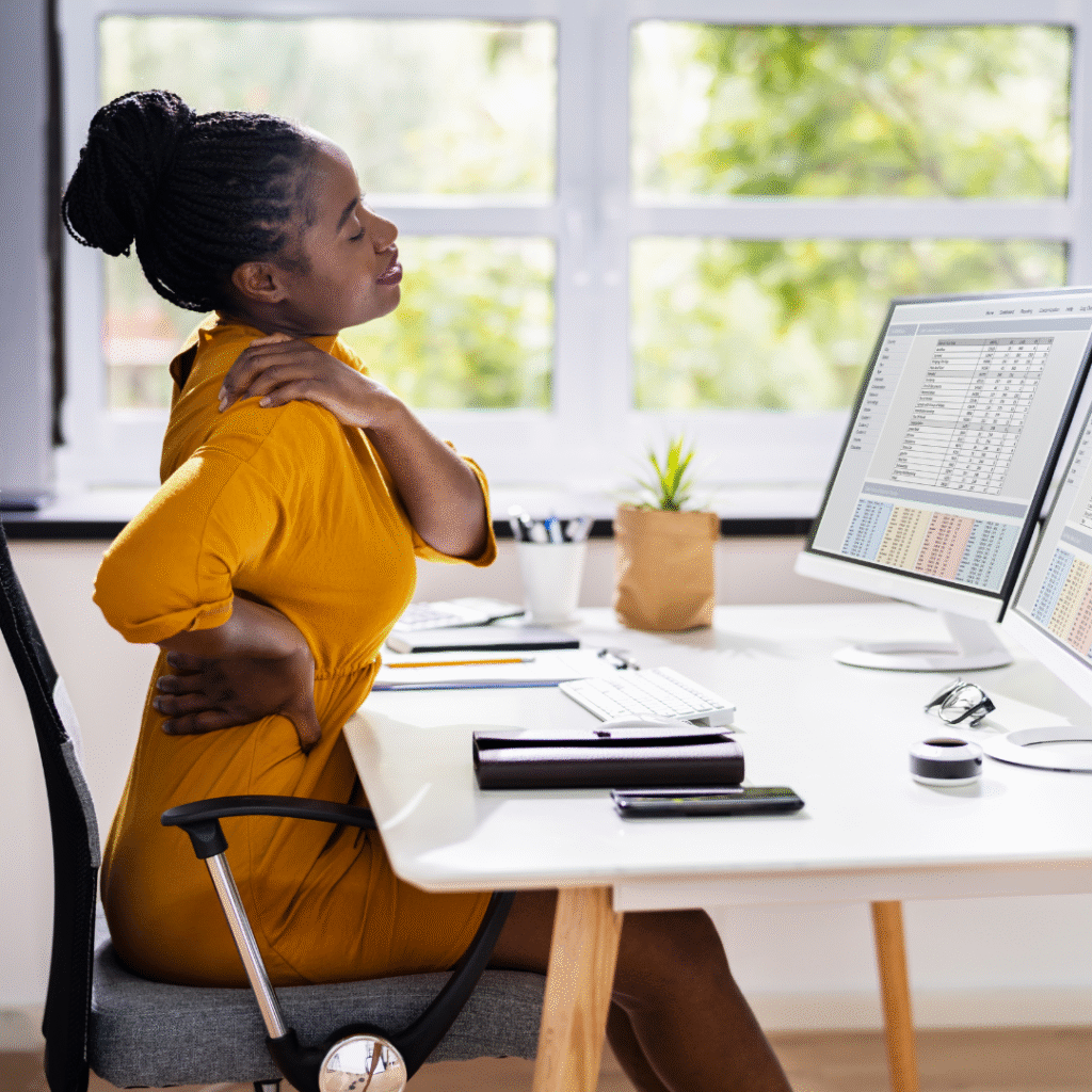 Black woman sitting at work desk with one hand on neck and another on lower back | how emotions are stored in the body