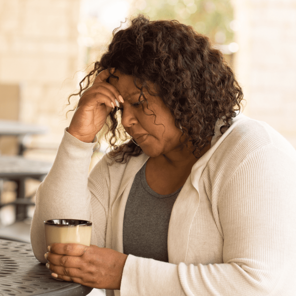 Older Black woman sitting at a table with coffee and head in hand | Can anxiety make you tired