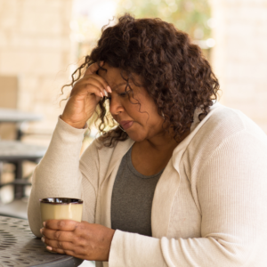 Older Black woman sitting at a table with coffee and head in hand | Can anxiety make you tired