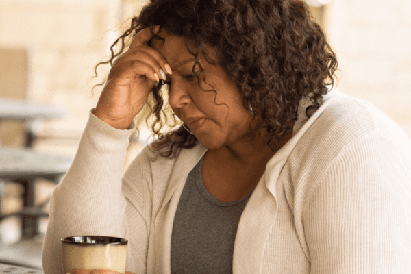 Older Black woman sitting at a table with coffee and head in hand | Can anxiety make you tired