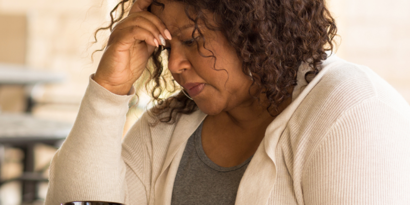Older Black woman sitting at a table with coffee and head in hand | Can anxiety make you tired