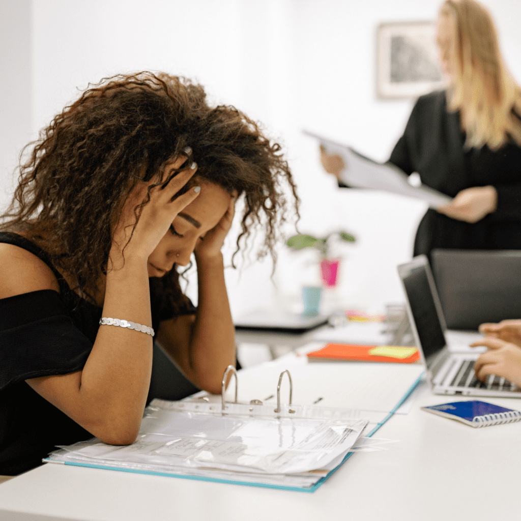 Young Black woman sitting at work, head in hands | why am i so tired all the time