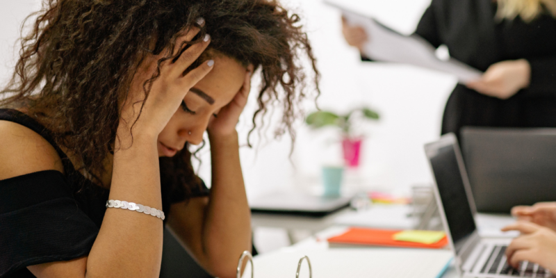 Young Black woman sitting at work, head in hands | why am i so tired all the time